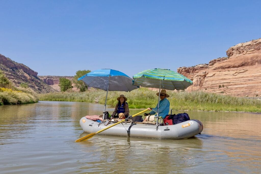 Two people sitting in packraft on Colorado River with two umbrella shading them from the sun