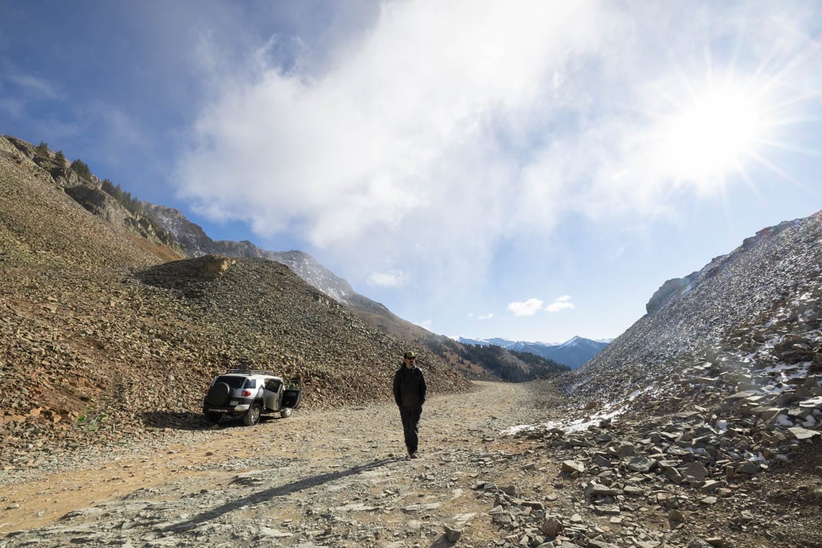 Man walking next to a FJ Cruiser at the top of Ophir Pass in Colorado