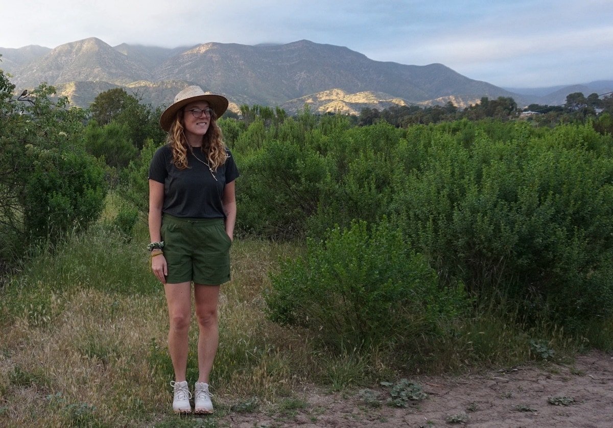 Woman wearing REI Co-Op Trailmade Shorts in green and Oboz Katabatic Trail Runners. She is smiling not looking at the camera.