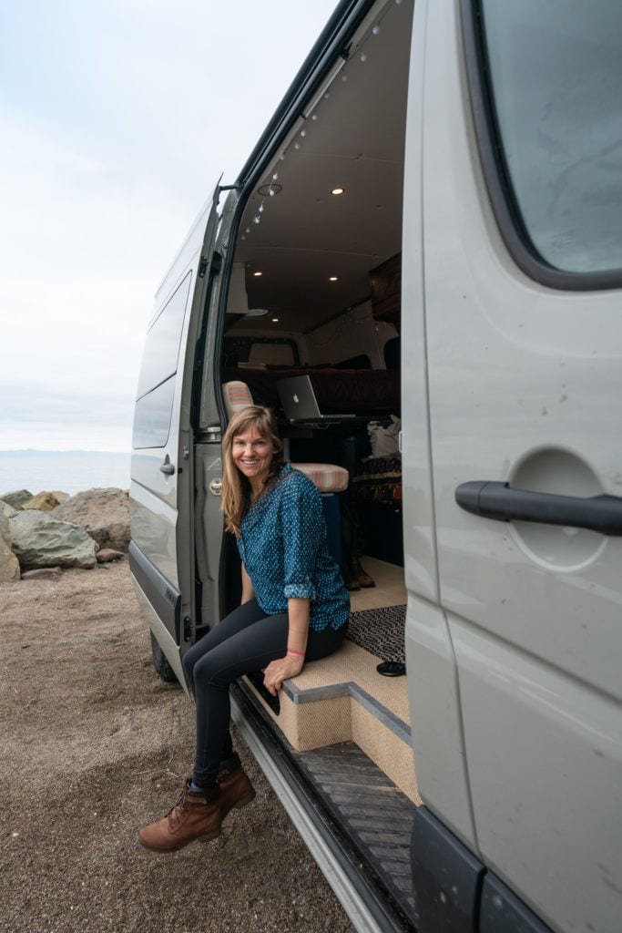 BFT Founder Kristen smiling with her feet dangling outside of her sprinter van in Santa Barbara