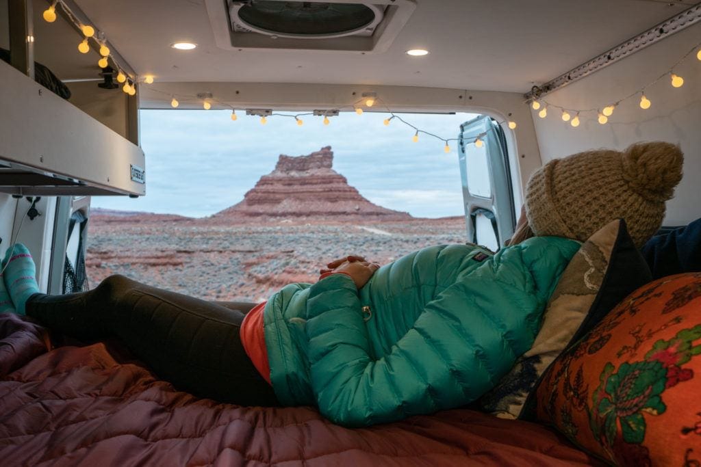 Kristen Bor lying in the back of a Sprinter van on the bed with red rocks background