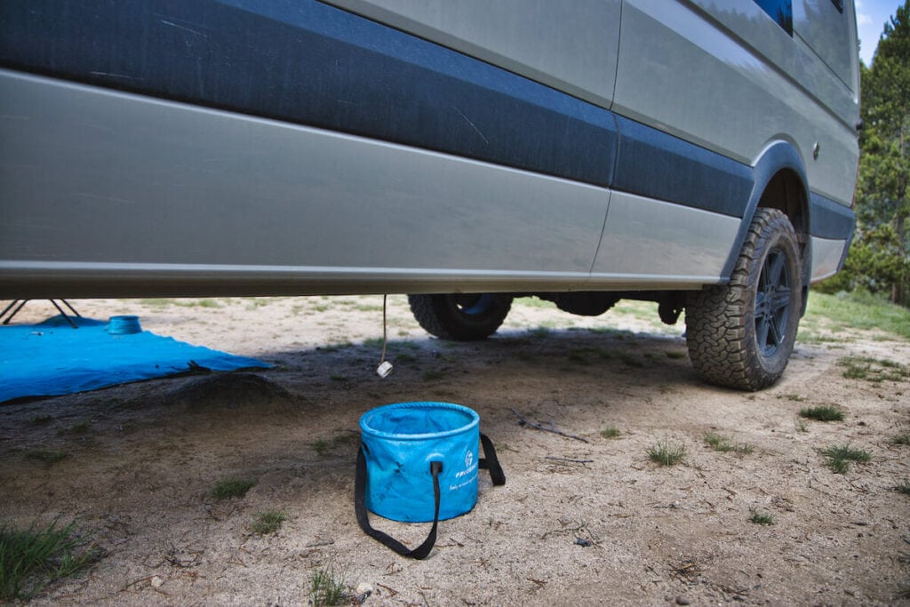 A collapsible bucket collects greywater underneath a sprinter van to follow Leave No Trace principles while campling