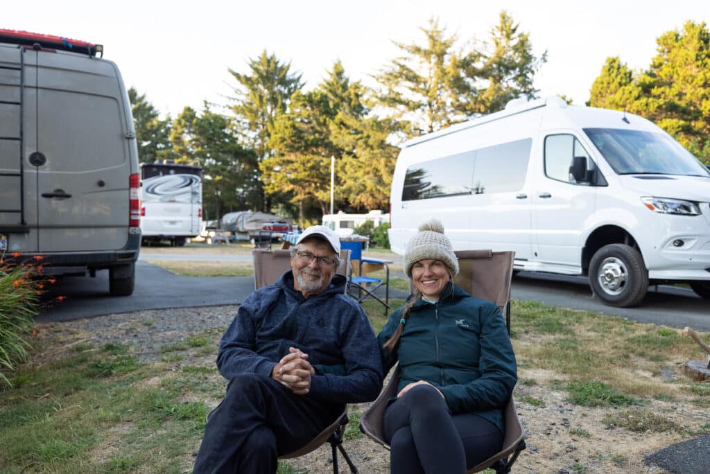 Bearfoot Theory founder Kristen Bor sitting in a camp chair next to her dad at a campsite with their Sprinter vans behind them