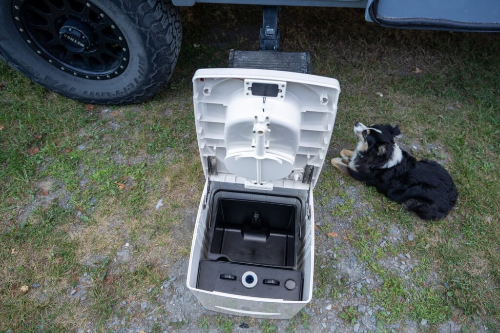 xKristen Bor demonstrating how to use the Compocloset Cuddy Lite composting toilet standing in front of a truck camper