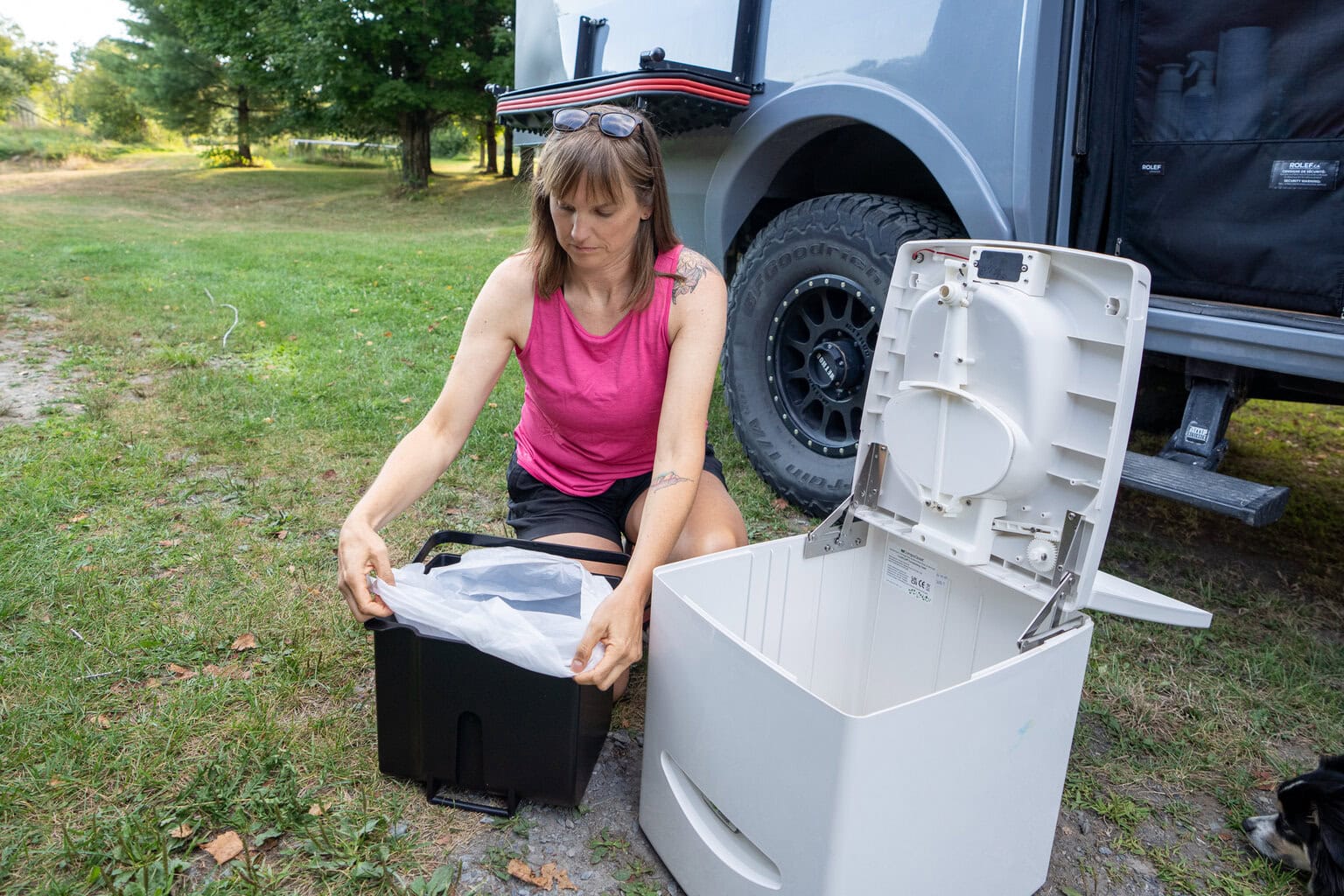 Kristen Bor demonstrating how to use the Compocloset Cuddy Lite composting toilet standing in front of a truck camper