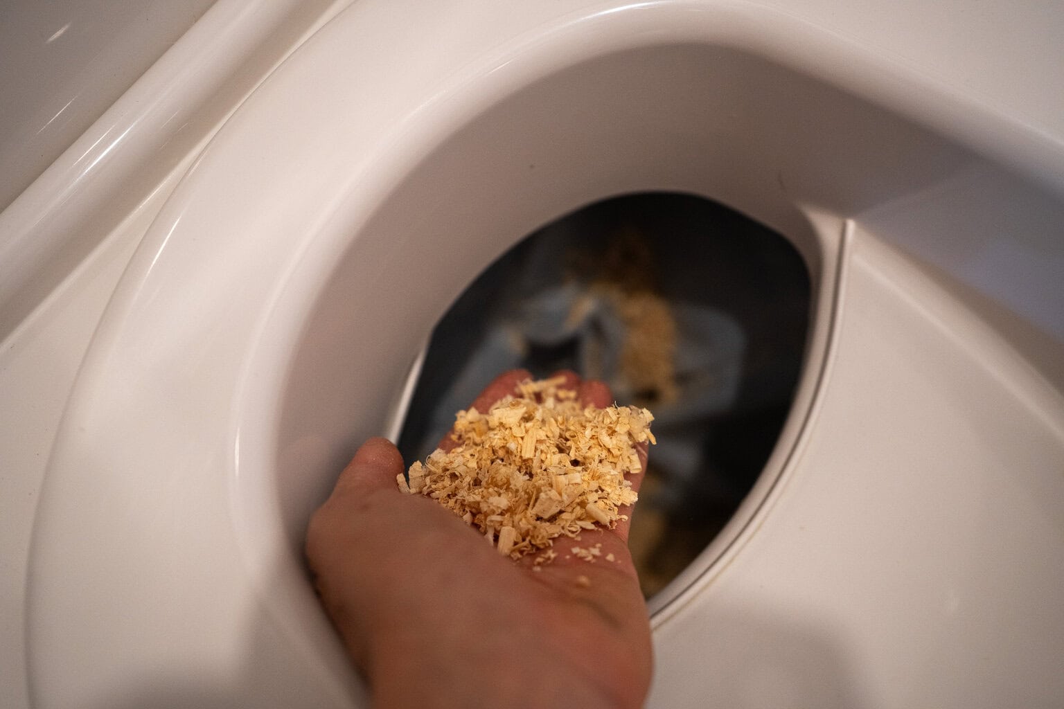Hand dropping wood chips into the solids bin of the Cuddy Lite toilet